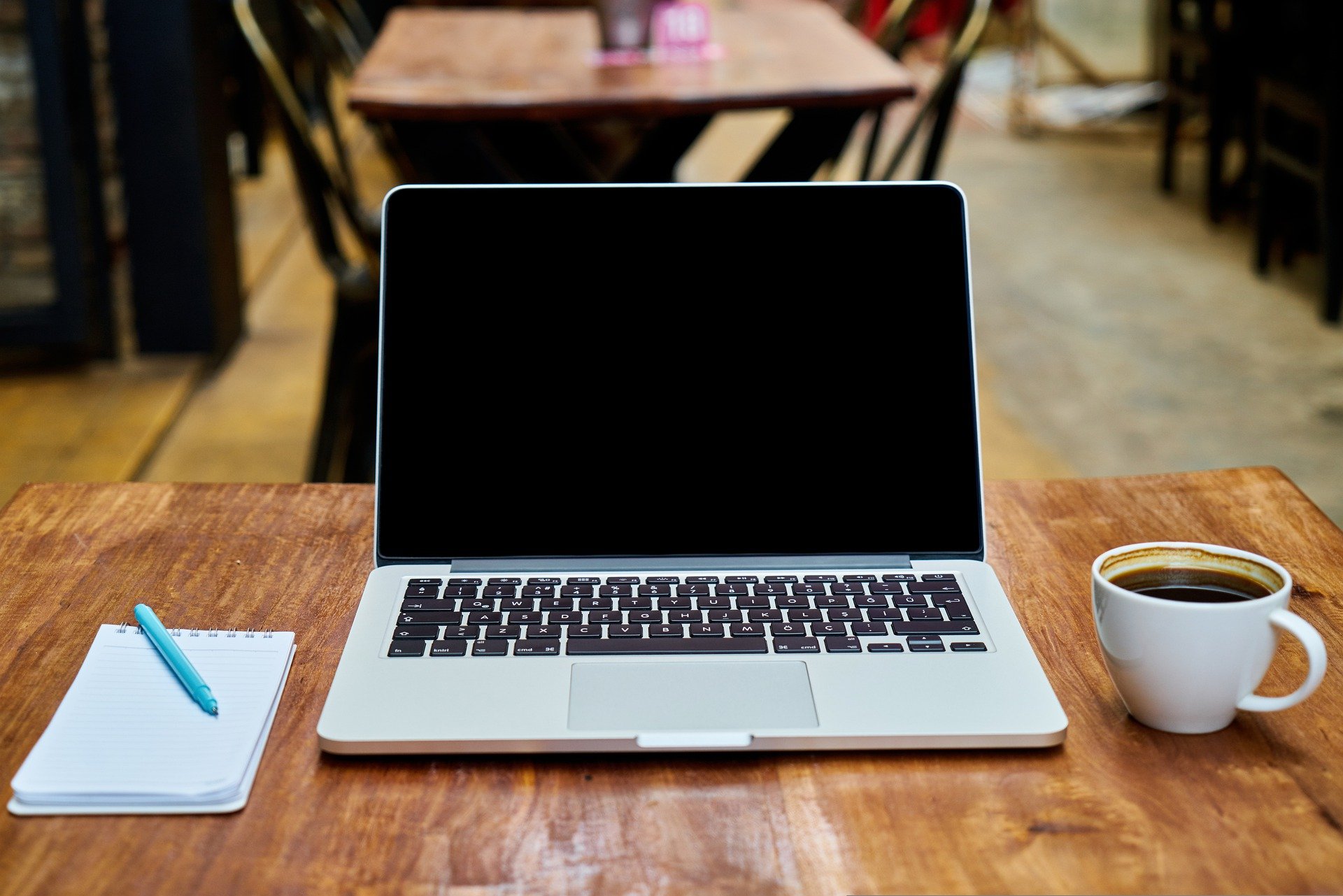 Stock photo of a laptop on a table with a notepad and cup of coffee