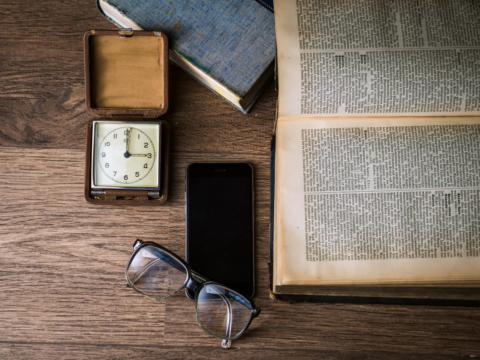 Stock photo of an open bible next to a phone, glasses, and pocketwatch